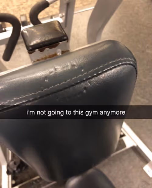 A portrait image of a backrest of a gym equipment almost about to blur, the start of the seat just starting at the lower end of the image. At the top of the backrest there are pock marks dug into the fabric almost as if someone has bitten it. There is a black translucent band across the image with white text saying “i’m not going to this gym anymore”.